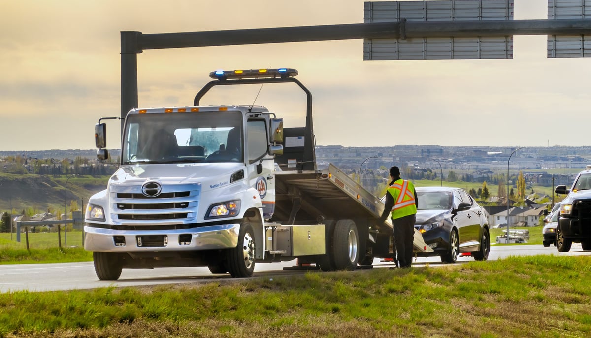 Tow truck driver assisting a broken-down sedan on a highway shoulder
